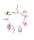A white pearl beaded charm bracelet with gold-tone metal settings and multiple decorative charms, including pink bow hearts, cherries, a lobster, and floral motifs, displayed on a white textured cushion.
