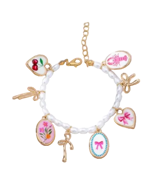 A white pearl beaded charm bracelet with gold-tone metal settings and multiple decorative charms, including pink bow hearts, cherries, a lobster, and floral motifs, displayed on a white textured cushion.